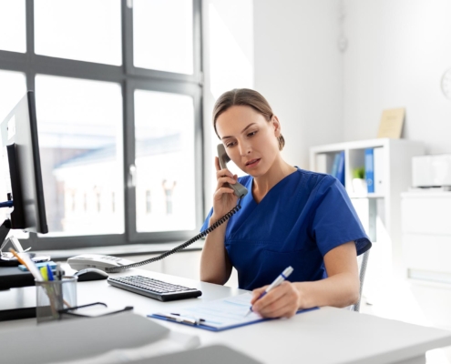 Image of a medical professional writing on a clipboard while on a phone call.
