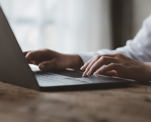 Side view of someone in a white longsleeved dress shirt typing on a laptop keyboard