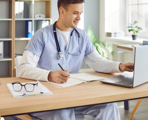 Front view of a young male doctor or nurse in blue medical uniform sitting at a desk