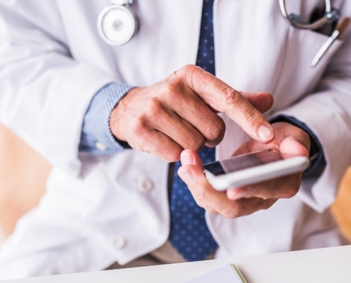 Senior doctor with smartphone working at the office.